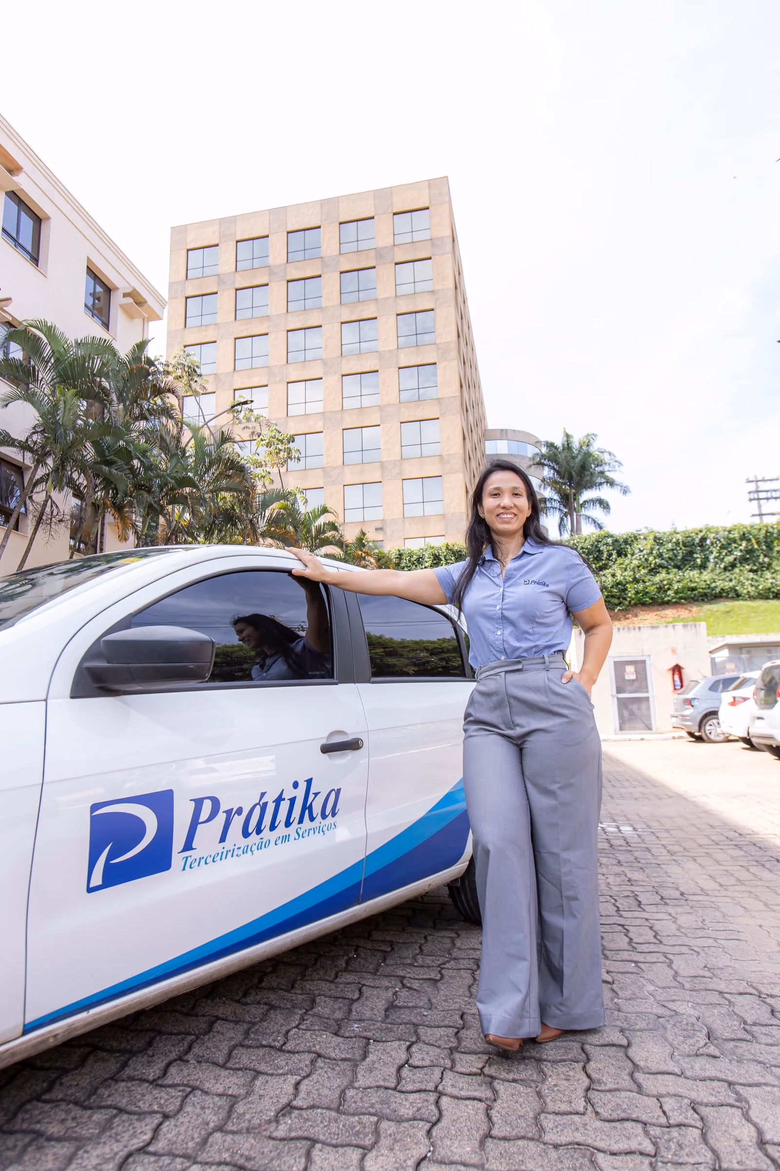 Supervisora da Prátika ao lado de um carro da frota própria, com prédios comerciais ao fundo