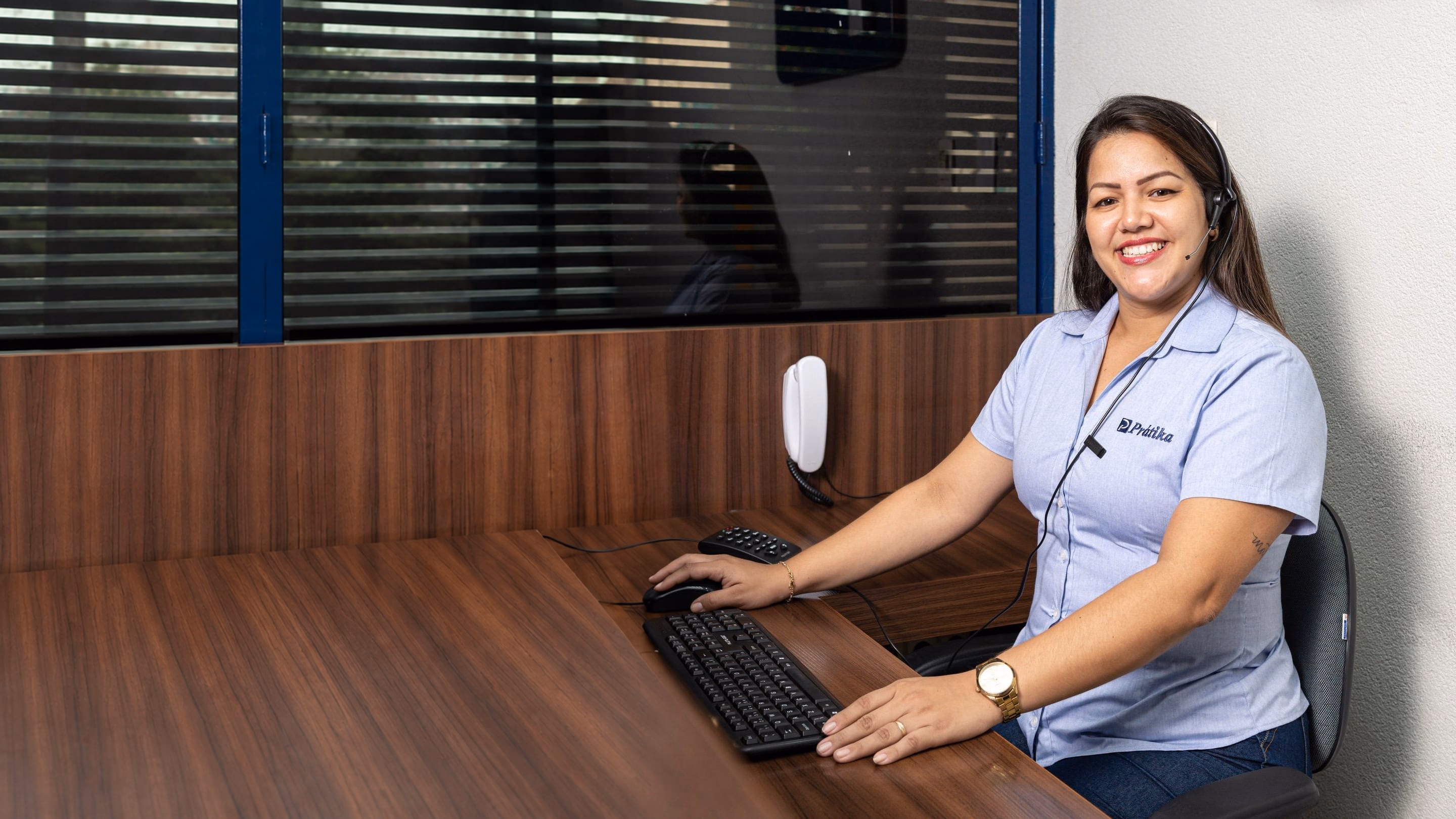 Atendente da Prátika sorri de headset, com as mãos no teclado, na central de atendimento