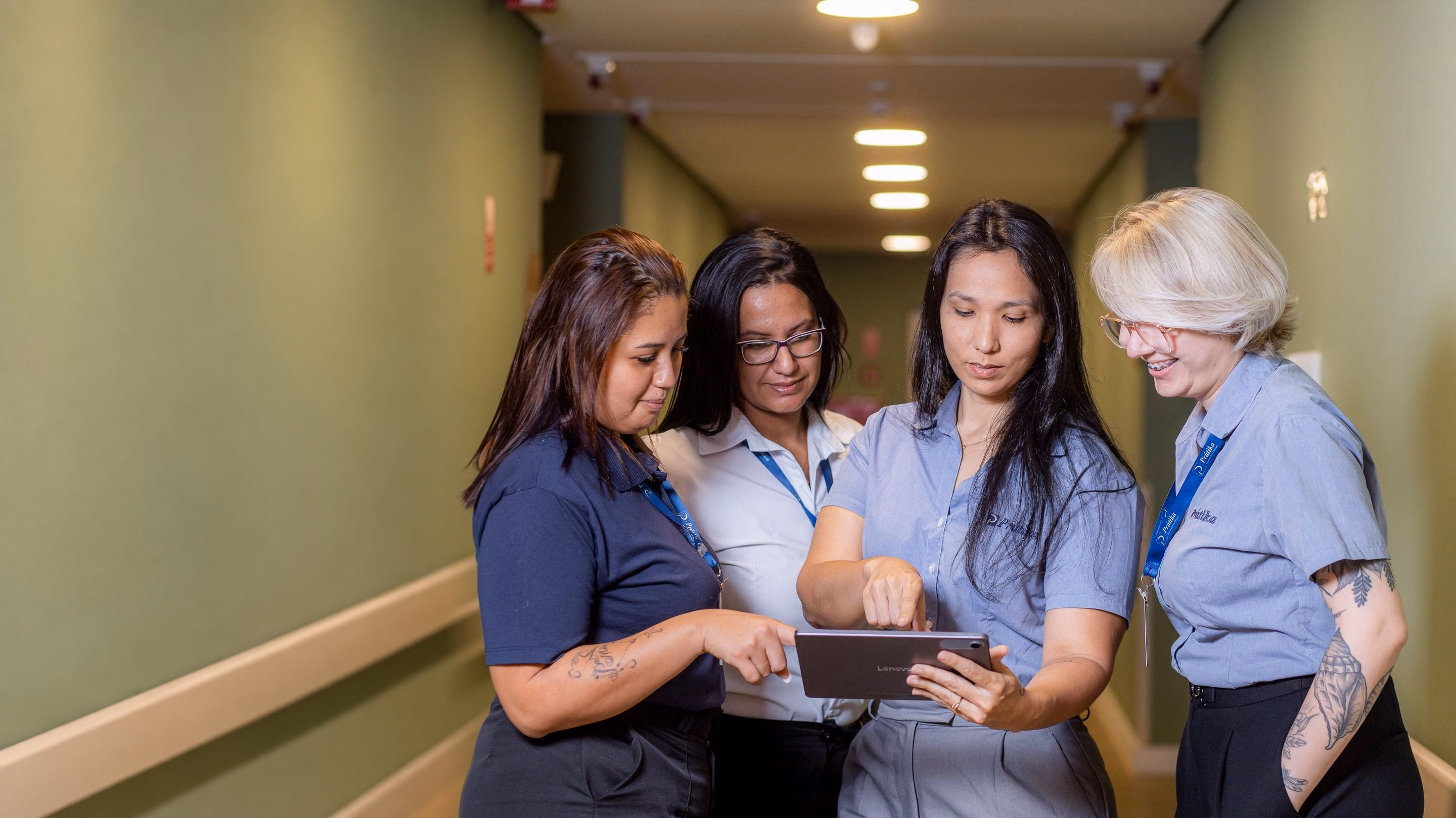 Quatro gestoras da Prátika conferem indicadores num tablet no corredor de um hospital