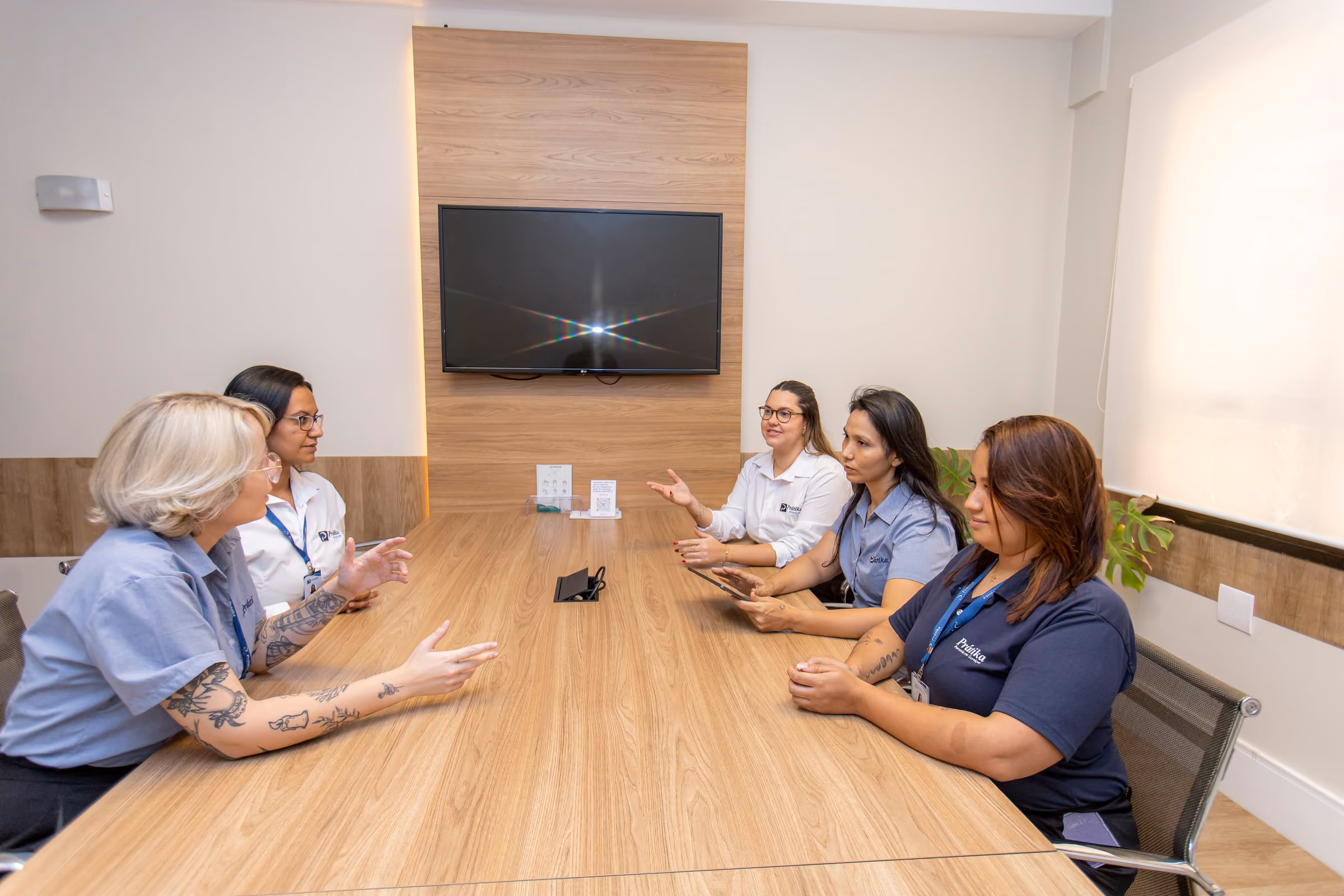 Cinco profissionais da Prátika conversam em reunião numa sala com mesa de madeira
